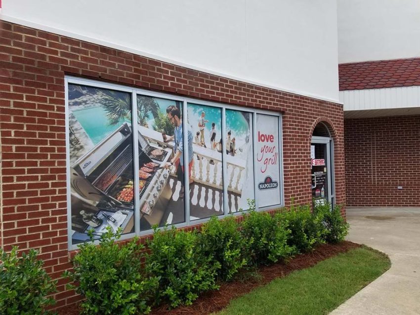 Window decals of man grilling while people sit near a pool.