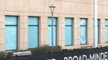 Side of building with light blue wall decals in front of a banner in grass. 