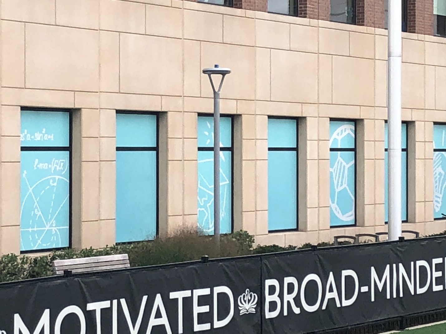 Side of building with light blue wall decals in front of a banner in grass. 