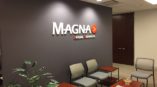 Office waiting room with chairs, a table and a plant in front of a dark wall that says Magna Legal Services in white.